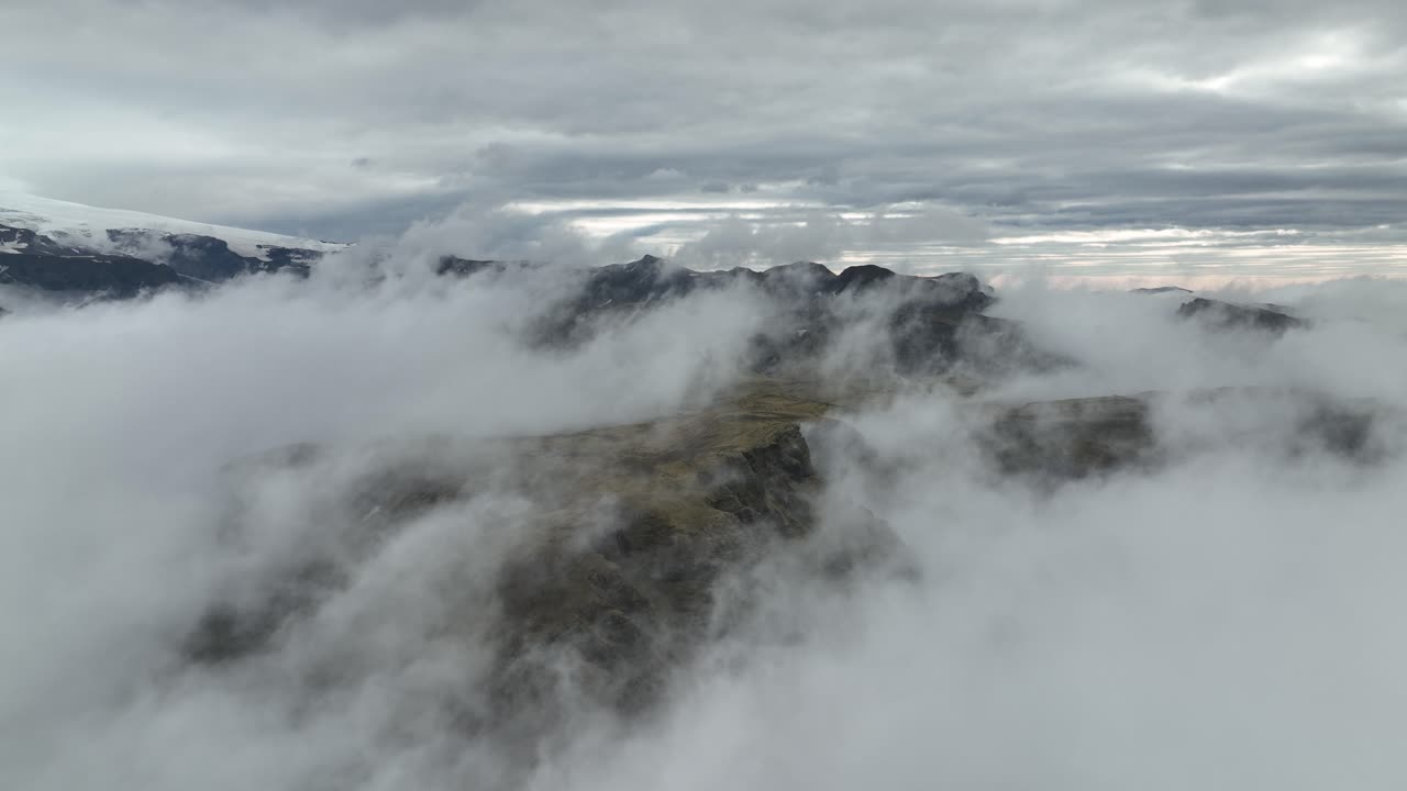 A dramatic aerial shot of fog rolling over mountain peaks in Hafursey, Iceland, with a moody sky and distant glaciers.