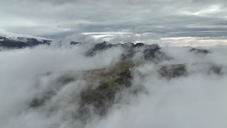 A dramatic aerial shot of fog rolling over mountain peaks in Hafursey, Iceland, with a moody sky and distant glaciers.