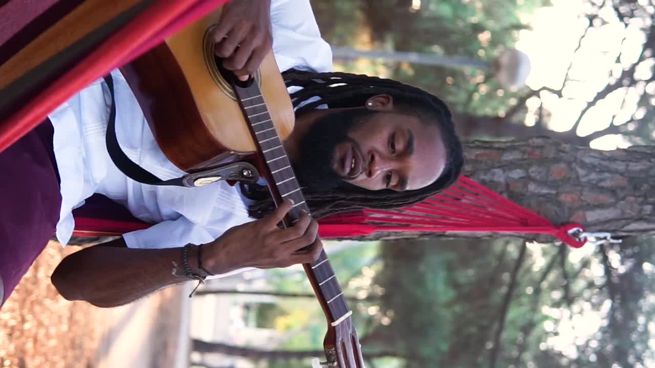 un tipo étnico tocando la guitarra en una hamaca en el campo