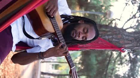 Ethnic-guy-playing-guitar-in-hammock-in-countryside