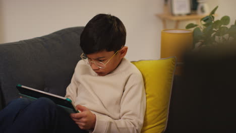 primer plano de un niño sentado en el sofá en casa jugando juegos o transmitiendo a una tableta digital 10