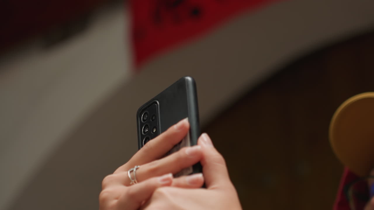 Primo piano di mani che tengono un telefono e registrano dal vivo a un evento, con anelli sulle dita. Sfondo del palco sfocato, profondità di campo ridotta, illuminazione serale calda. Prospettiva autentica del pubblico che cattura il momento per i social media.