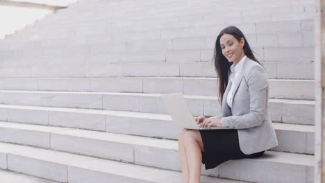 Smiling-woman-using-laptop-on-stairs