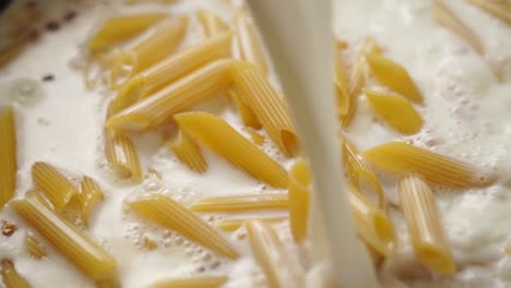 anonymous cook adding cream into frying pan with macaroni