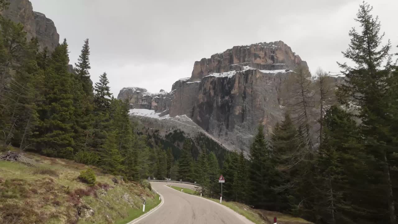 Warning signs mark a sharp curve on Giau Pass as the winding road stretches ahead into the Dolomites, framed by towering alpine peaks and dramatic terrain