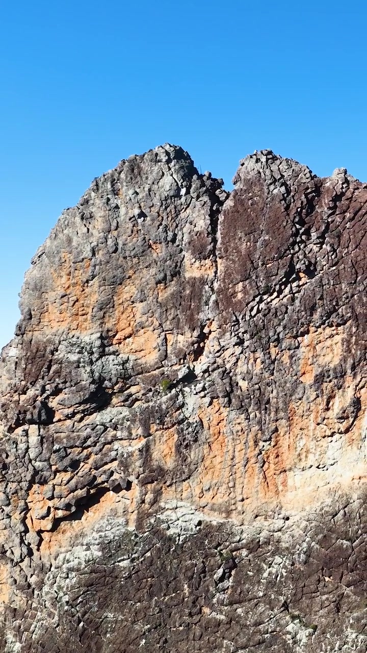 Zoom lento hacia acantilados volcánicos texturizados bajo cielos azules despejados en el Parque Nacional Warrumbungle