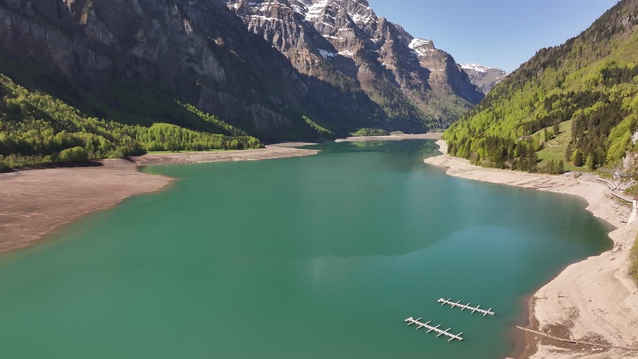 The glacial-fed, turquoise Klöntalersee in Glarus, Schweiz, is dwarfed by towering, snow-capped Alpine peaks. Concept of rugged natural majesty