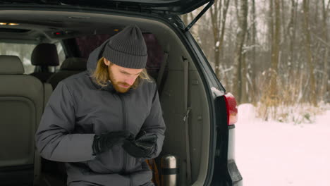 guapo hombre barbudo sentado en el maletero del coche y usando el teléfono móvil en un día de invierno nevado 1