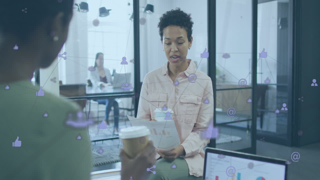 Animation of connected icons over diverse female coworkers discussing reports while drinking coffee