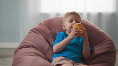 toddler boy eats puff pie sitting in bean chair at home