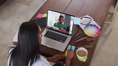african american female teacher writing on memo notes while having a video call with a boy on laptop