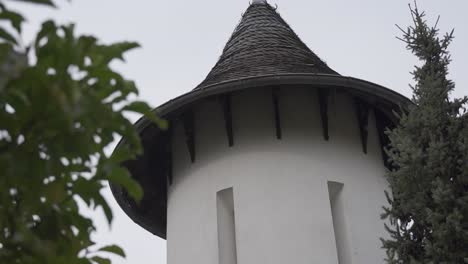 small white tower with pointed roof and oblong windows between trees