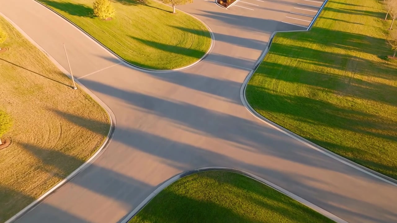 An aerial view of a calm and serene urban park setting, showcasing curved pathways and lush green grass. The scene features a mix of natural and concrete elements, with brown and white hues.