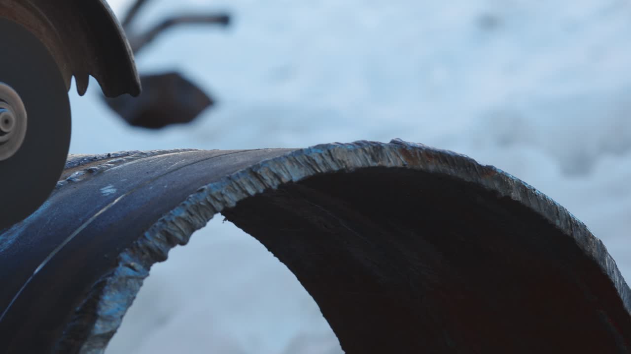 The angle grinder cuts a large-diameter metal pipe and sparks fly. Close-up of work in production.