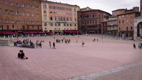 big square with old buildings and people walking in tuscany, italy on a cloudy day.