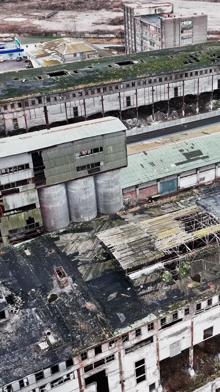 Neglected locality of a past time plant. Abandoned ruins of warehouses with broken walls, windows and roofs. Aerial view. Vertical video