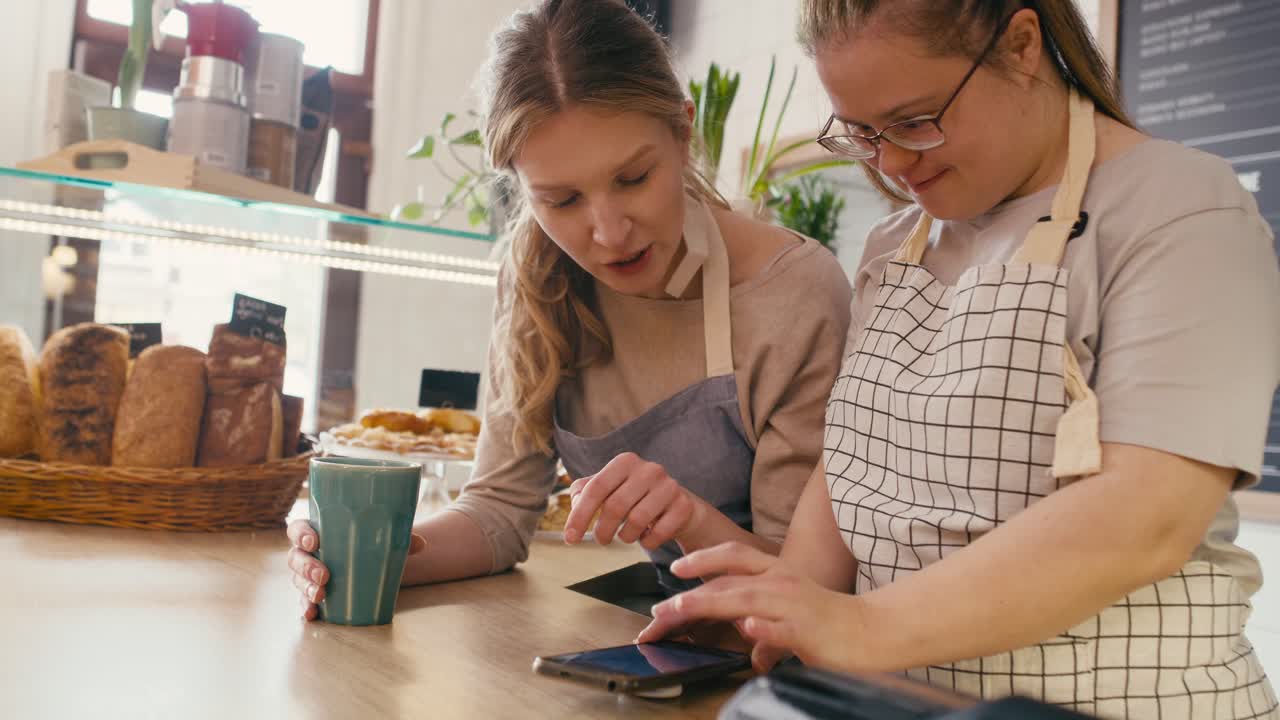 chica con síndrome de down navegando por teléfono junto con su compañero de trabajo en el café
