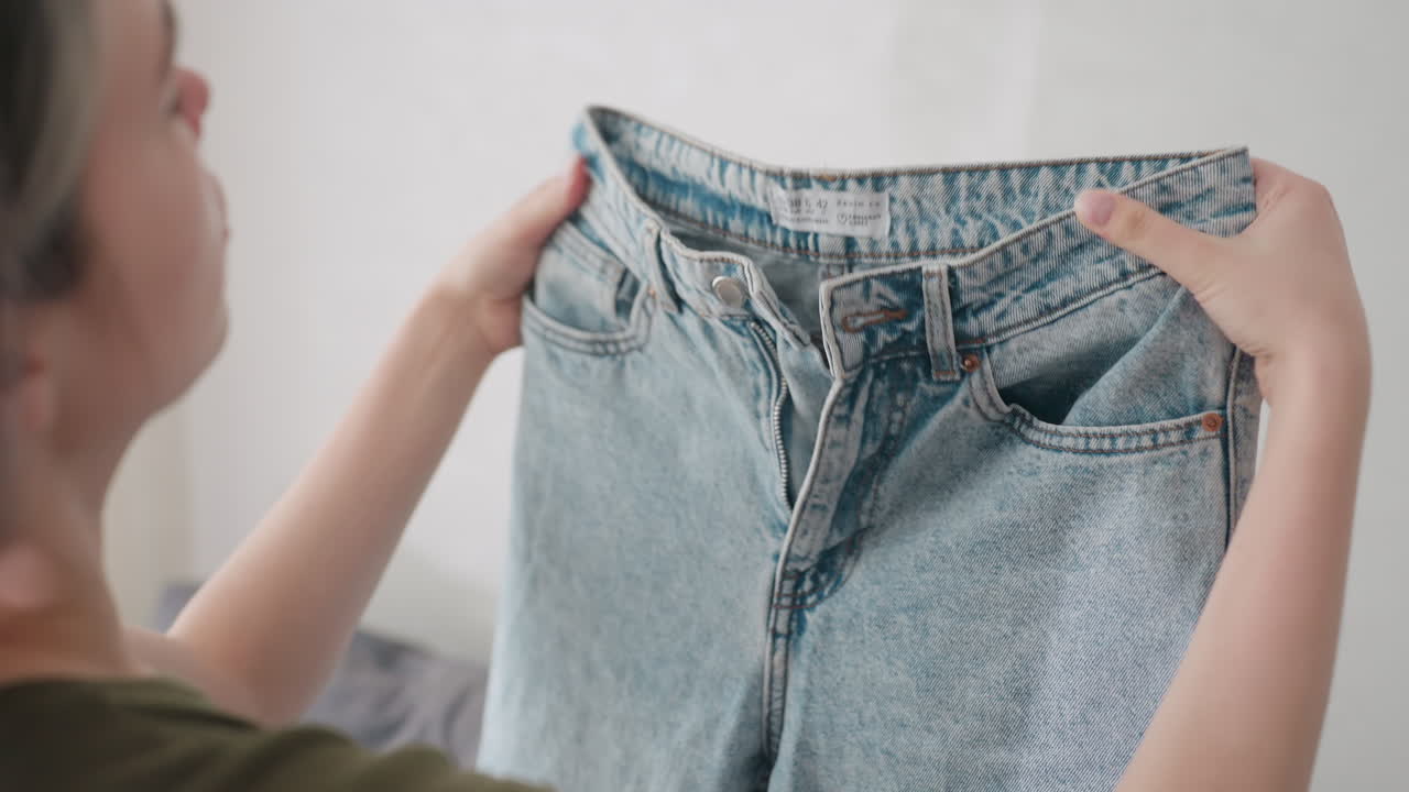 Extreme close up hand view of lady gently folding jeans trouser with care showing detail of denim texture domestic routine clothing maintenance lifestyle responsibility and household activity