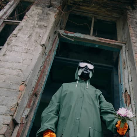 flowers in hand of an ecologist in protective suit. person in respirator and hazmat wearing standing with flowers in ruined place. nature in danger