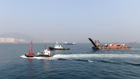 Barge-loaded-with-Concrete-mixer-trucks-pulled-to-port-by-a-Tugboat-in-Hong-Kong-bay,-Aerial-view