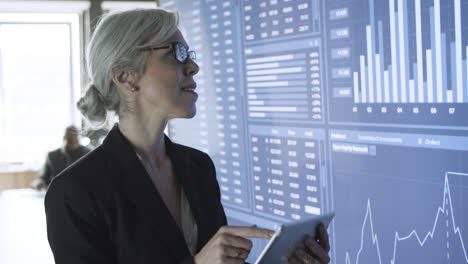 middle-aged content businesswoman using tablet and standing in front of a screen