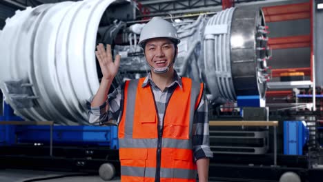 asian male engineer with safety helmet smiling to camera and waving hand saying bye while standing with airplane engine maintenance conducted, analytics checking the turbine
