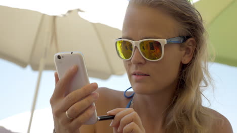 mujer con gafas de sol usando celular en la playa