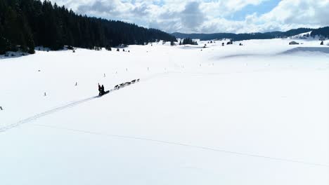 Toma-De-Seguimiento-De-Drones-De-Un-Trineo-Tirado-Por-Perros-En-Un-Hermoso-Valle-Nevado-Con-Dos-Mushers-Felices