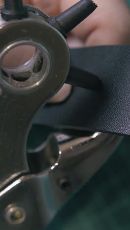 cu: experienced workshop worker makes holes in black leather belt with special silver punch pliers extreme closeup