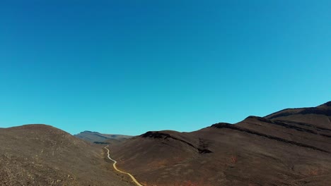 4K-Drohnenaufnahme-Aus-Der-Luft,-Die-Berge-Und-Unbefestigte-Bergpässe-Mit-Klarem-Blauen-Himmel-Zeigt