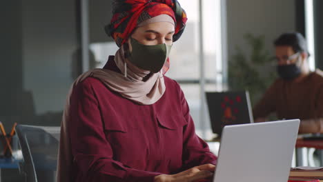 funcionária de escritório em hijab e máscara trabalhando em laptop