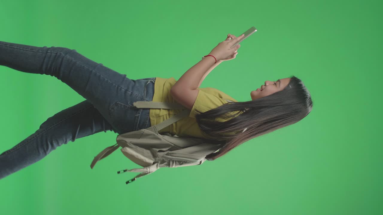 vista lateral de una estudiante asiática que usa una tableta y camina a la escuela en una pantalla verde