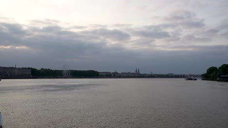 View-of-the-Garonne-river-in-Bordeaux-France-at-dusk-with-Quinconces-Ferris-wheel-in-the-distance,-View-from-boat