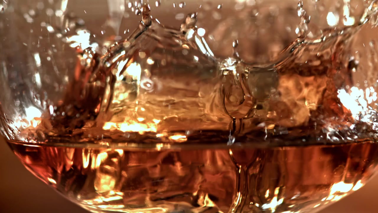 Cubetto di ghiaccio che cade in un bicchiere di whisky al rallentatore