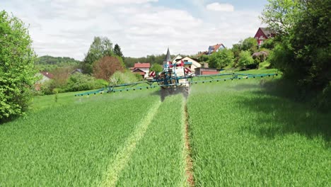 Ein-Traktor,-Der-Chemikalien-Auf-Einer-Grünen-Wiese-Versprüht,-Fährt-Auf-Gebäude-Zu