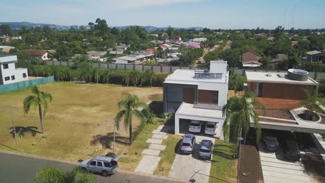 beautiful houses with concrete and glass wallings surrounded by lush palm trees in ponta da figueira, brazil, cars parked at the garage on a hot sunny weather - aerial shot