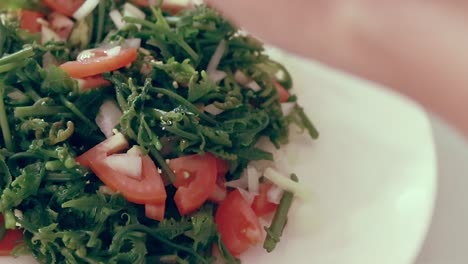 Toma-En-Primera-Persona-De-Una-Mano-Añadiendo-Condimentos-A-Un-Plato-De-Helecho-Fiddlehead-O-Ensalada-De-Pako,-Un-Manjar-Local-Filipino-Que-Muestra-La-Auténtica-Vida-Hogareña-Y-El-Patrimonio-Cotidiano