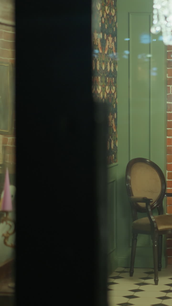 두 개의 의자와 테이블이 있는 편안한 방으로 유리 문을 닫는 손의 모습. 드 헬드 카메라로 촬영되어, 들리어, 미술품 및 빈티지 장식으로 방의 매력적인 분위기를 포착합니다.