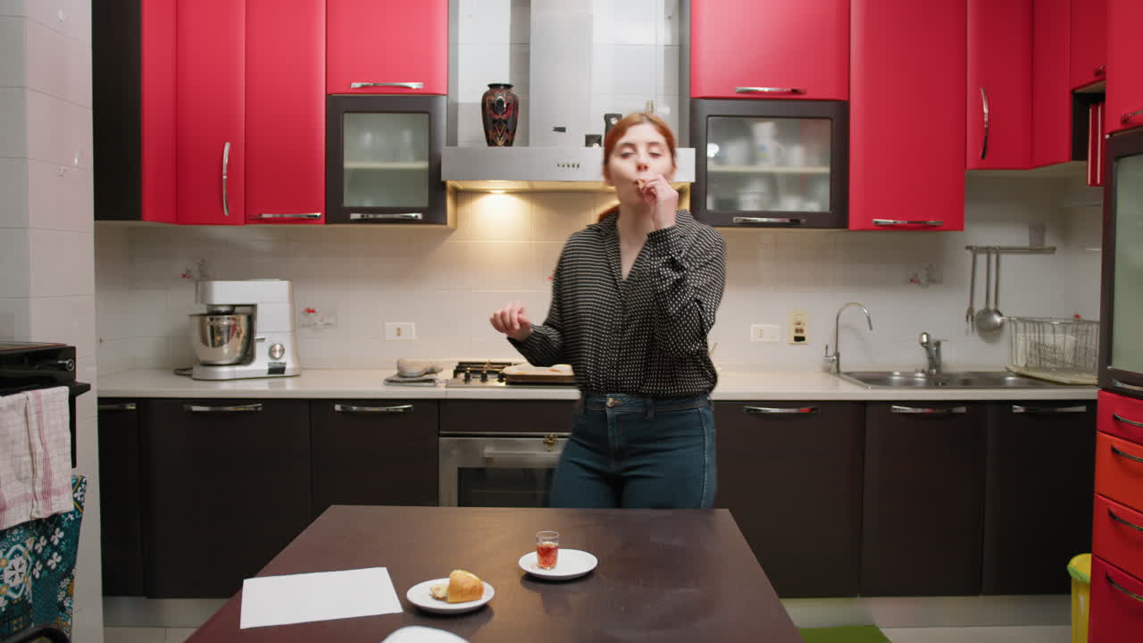 Nella cucina di casa sua una donna balla e canta mentre fa uno spuntino.