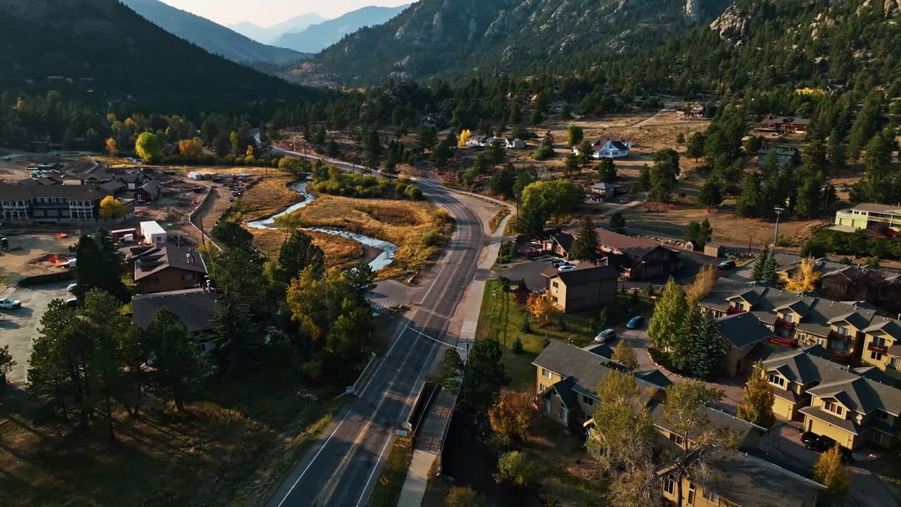 Drone trucking pan orbit over Estes Park, Colorado, showcasing mountain roads winding through fall foliage with soft sunlight