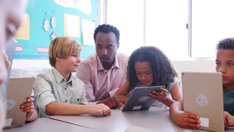 male teacher helping elementary school kids using tablet