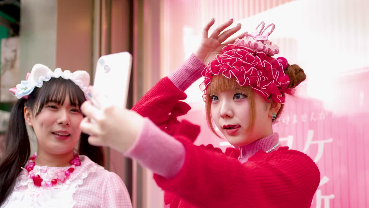 Due donne in vivace stile decora street rosa si scattano selfie con uno smartphone a Tokyo