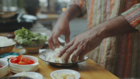 close-up of hands of man coating cubes of paneer cheese with flour