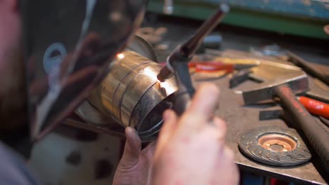 Young-skilled-man-wearing-welding-mask,-gas-welding-exhaust-tube-together