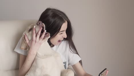 Una-Chica-Encantadora-Con-Aparatos-Ortopédicos-Juega-Con-Su-Mascota,-Que-Es-Un-Labrador-Blanco,-Y-Trata-De-Hacer-Selfies-Juntos