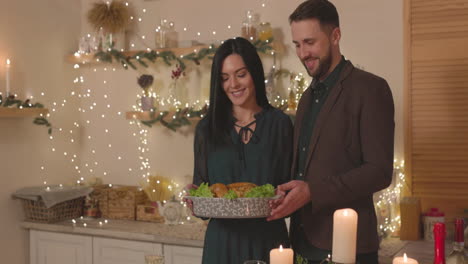 pareja elegante poniendo pollo asado en la mesa de la cena de navidad