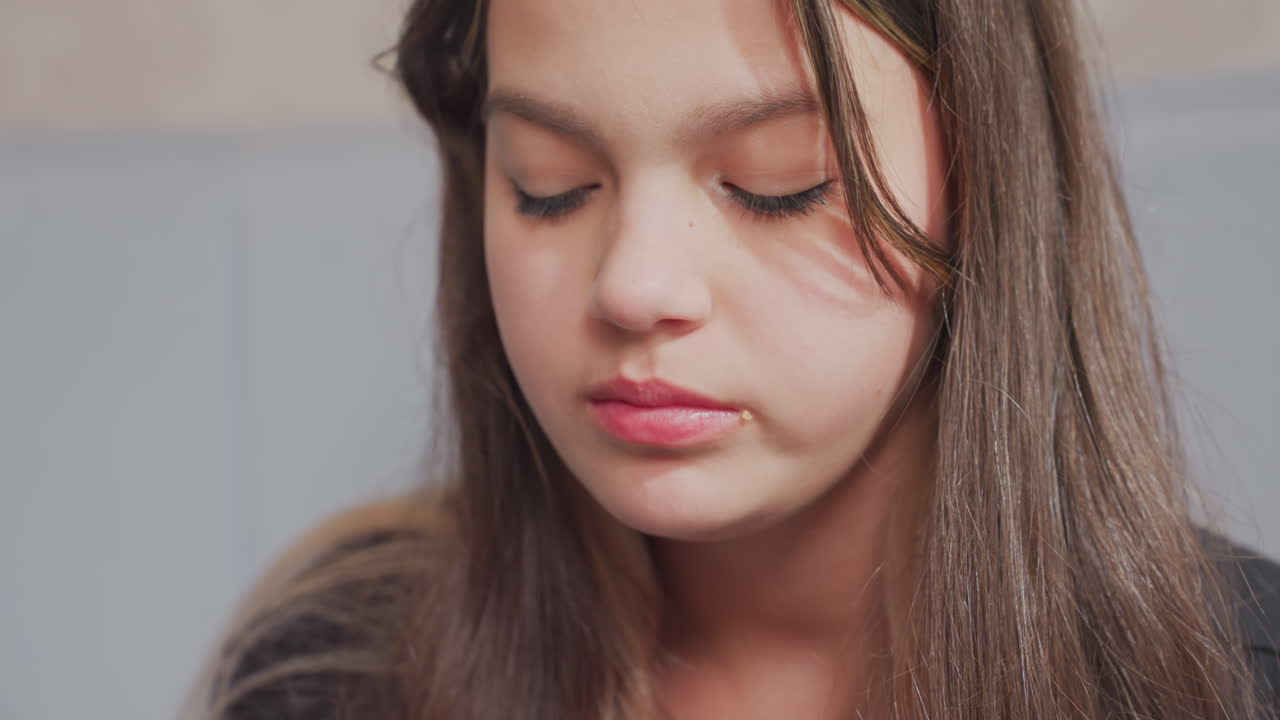 Close up side view of young girl eating potato chips with focused expression indoors, crumbs visible near mouth as she chews snack, showcasing natural behavior in casual, relaxed setting