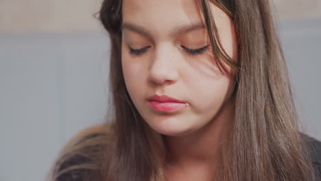close up side view of young girl eating potato chips with focused expression indoors, crumbs visible near mouth as she chews snack, showcasing natural behavior in casual, relaxed setting