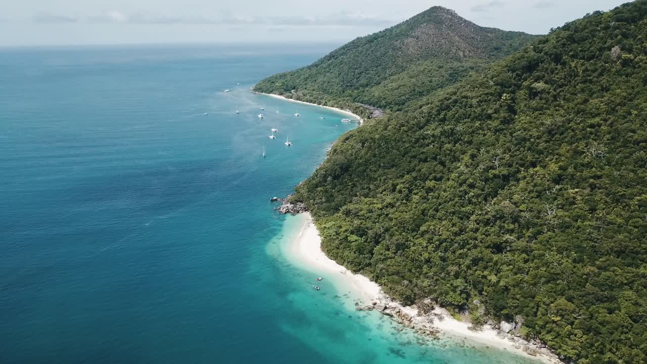 antenas de drones bajan y giran alrededor de una isla tropical de aguas azules claras en un día soleado con reflejos de nubes