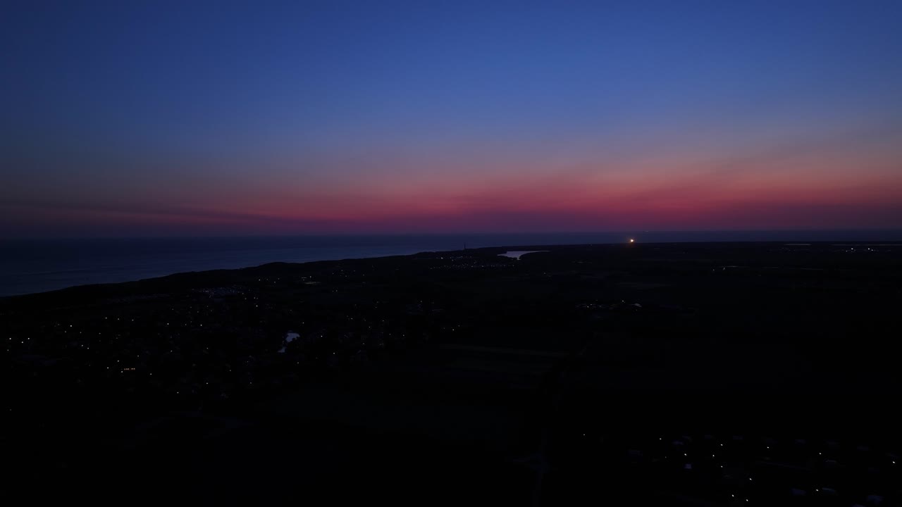 네덜란드 해안선 위의 다채로운 일몰 후 지평선에서 박이는 등대